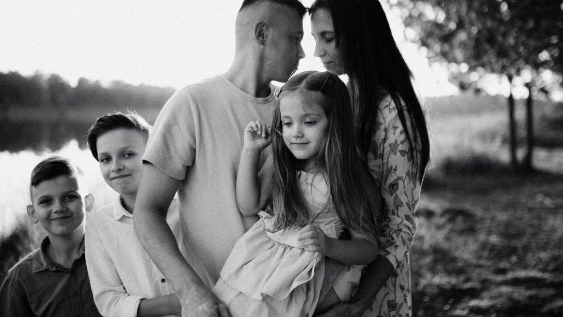 A serene black and white portrait of a family standing by a lake.